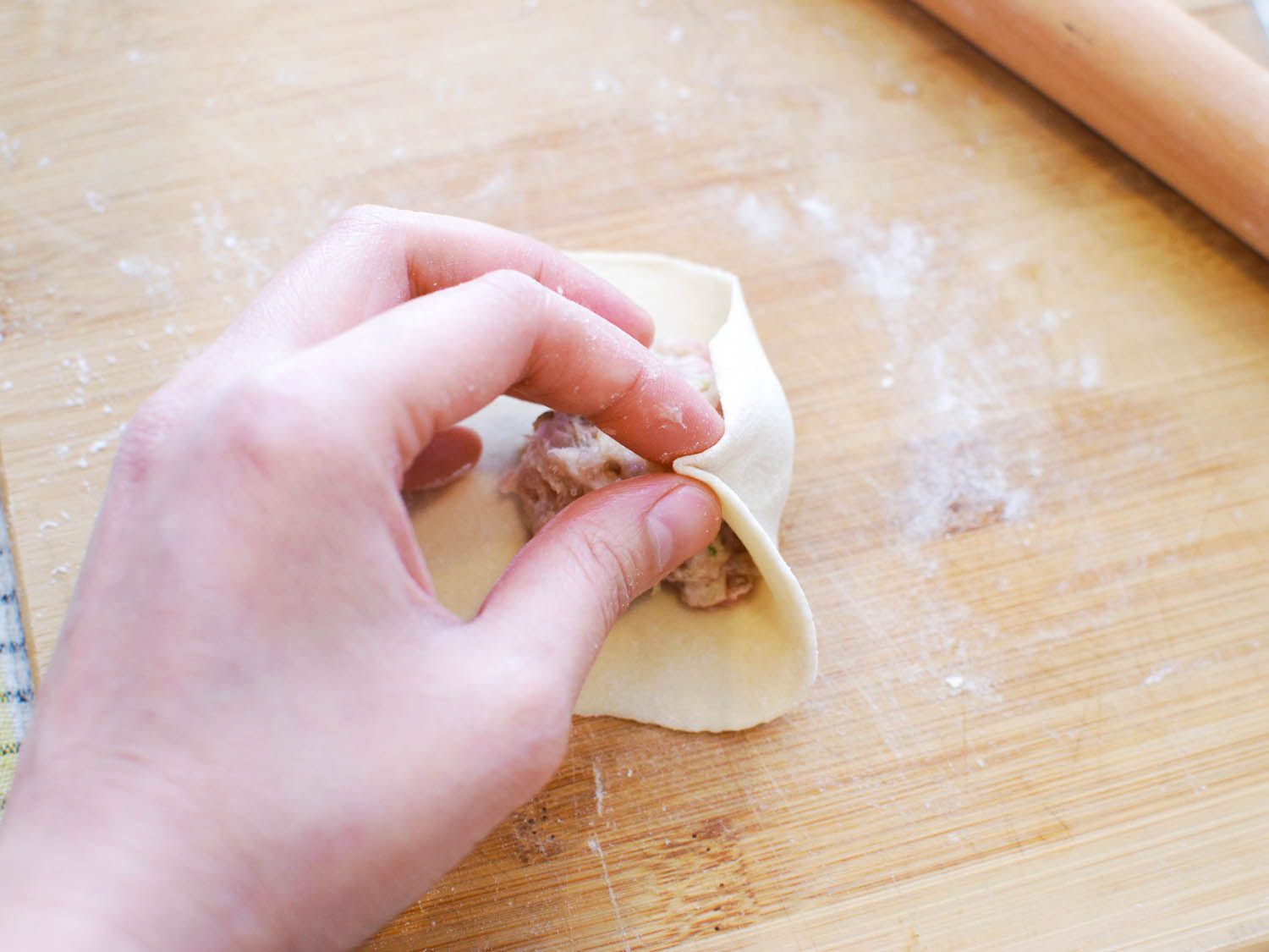 Pinching the sheng jian bao wrapper to form a pleat.