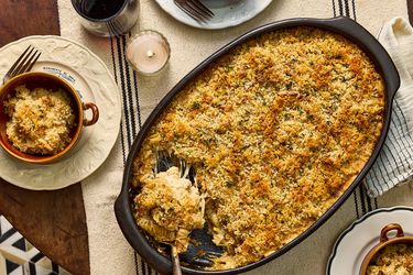 Large dish of French onion soup mac and cheese, with 2 cups of servings on dishes, a candle, a striped tablecloth