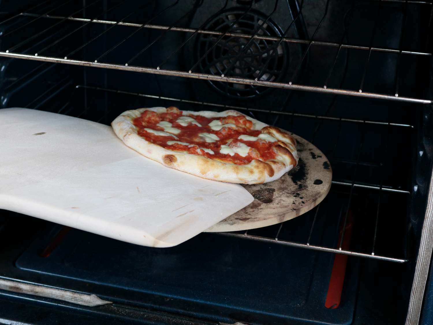 A wooden peel turning a pizza in an oven
