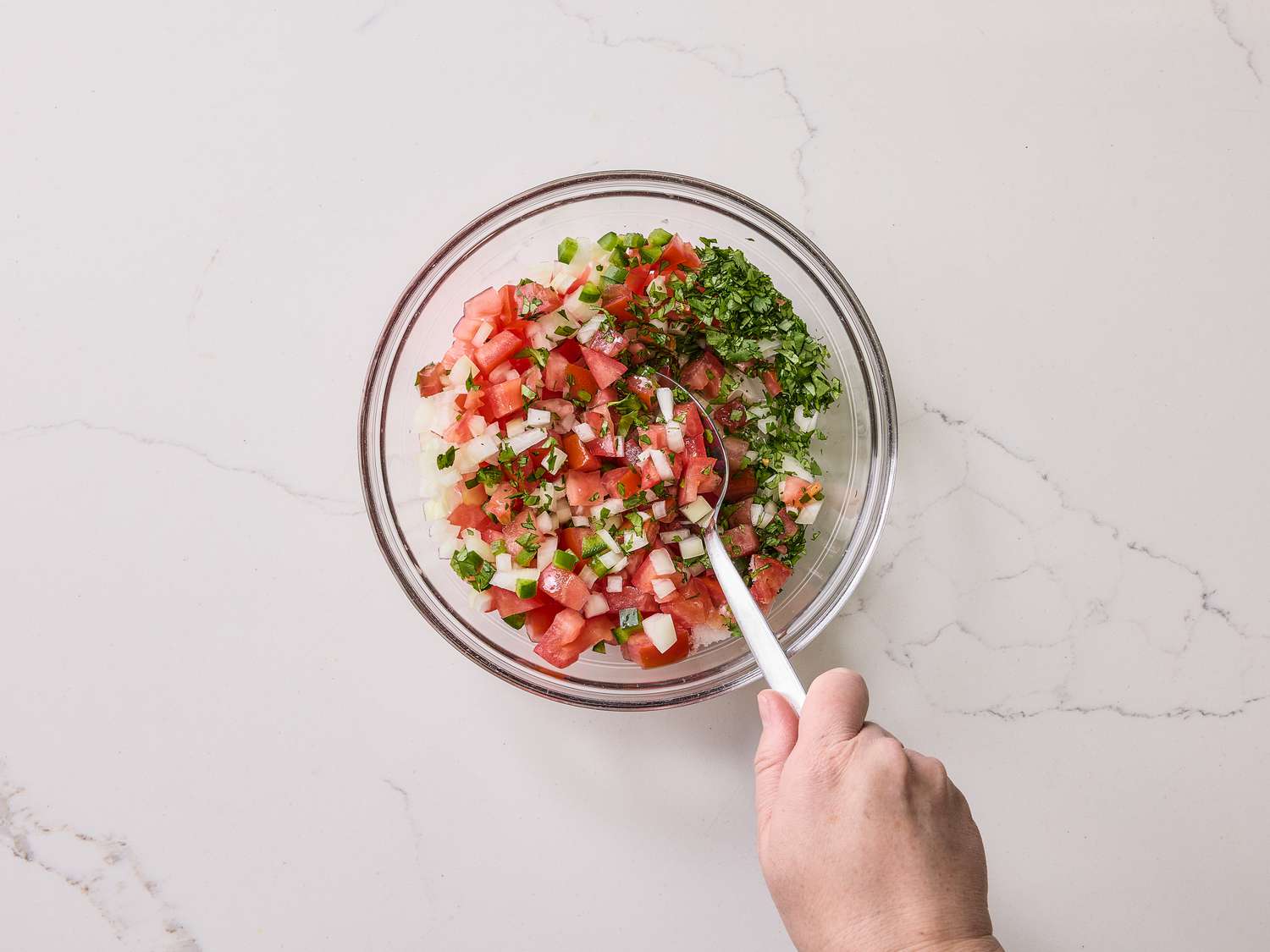 Mixing together pico de gallo ingredients in a small glass bowl 