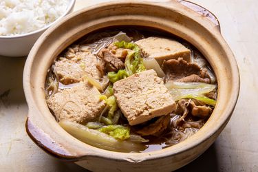 A clay pot filled with Frozen Simmered Tofu Soup with Pork, Cabbage, and Rice Noodles with rice alongside