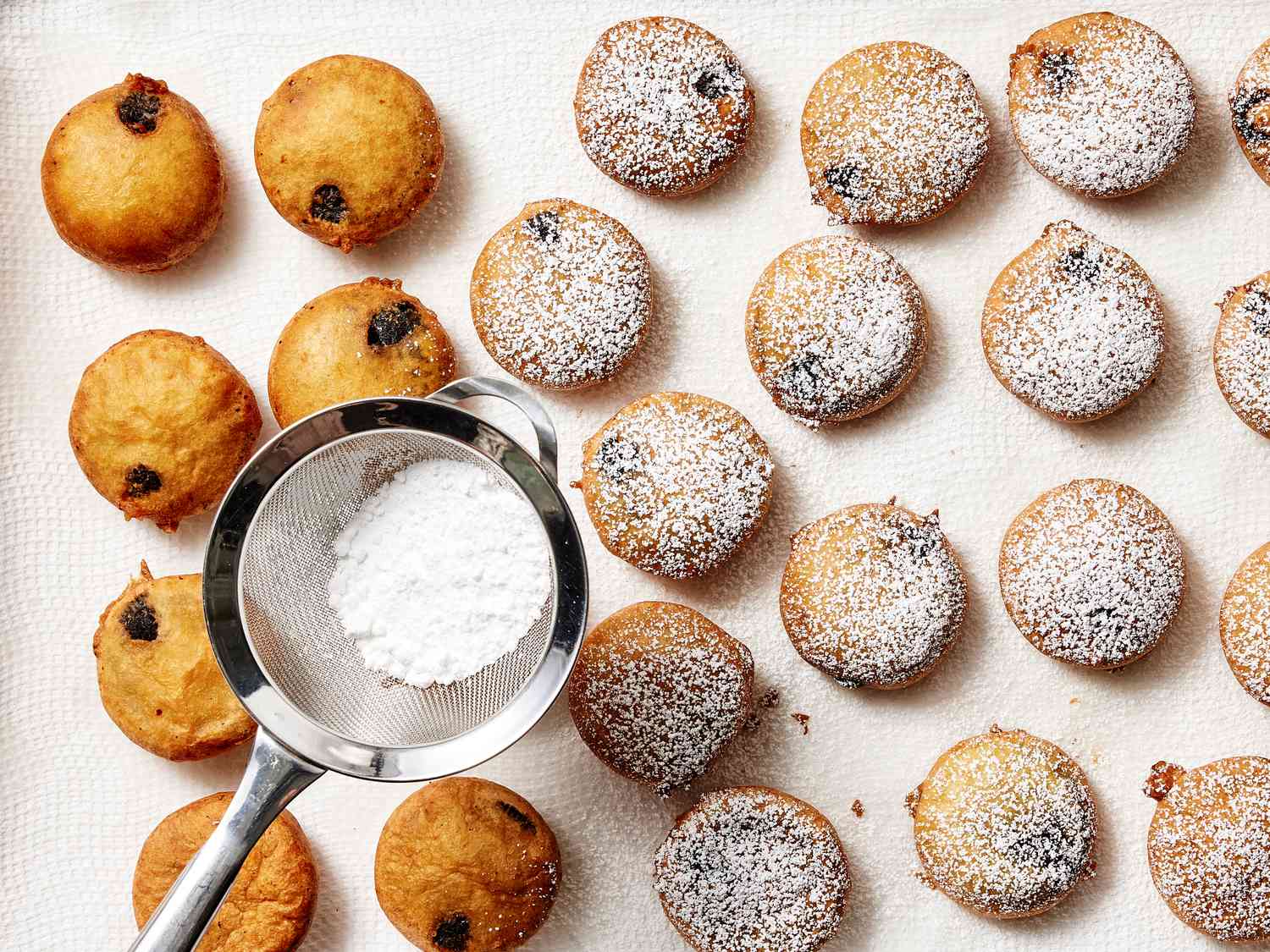 cookies on a paper towel lined sheetpan, being dusted with powdered sugar