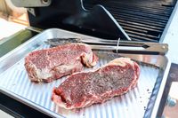 Two raw Butcherbox steaks with seasoning on a tray next to a grill