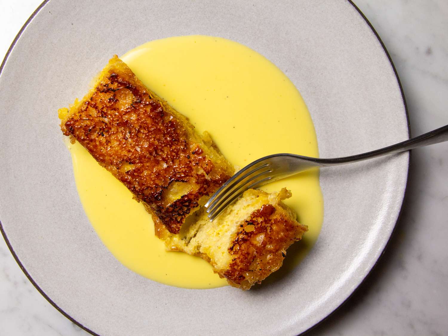 A slice of torrijas caramelizadas, Spanish-style caramelized custard-soaked toast, on a plate served with crème anglaise. 
