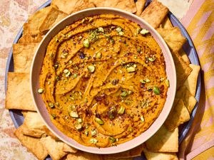 A bowl filled with a creamy zatar carrot dip garnished with chopped pistachios, accompanied by pita chips