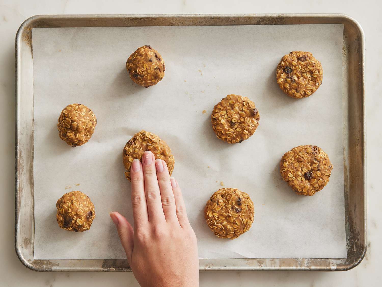 Hands flattening dough into one inch tall discs on a parchment paper lined baking sheet 