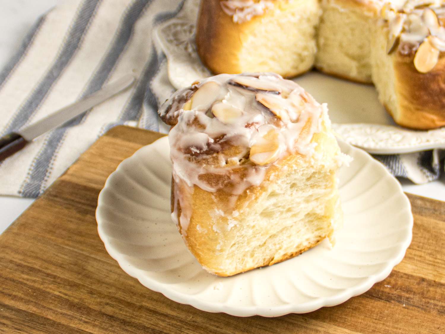 almond frangipane roll on white plate on wooden board, with rolls on background, and a striped napkin. 