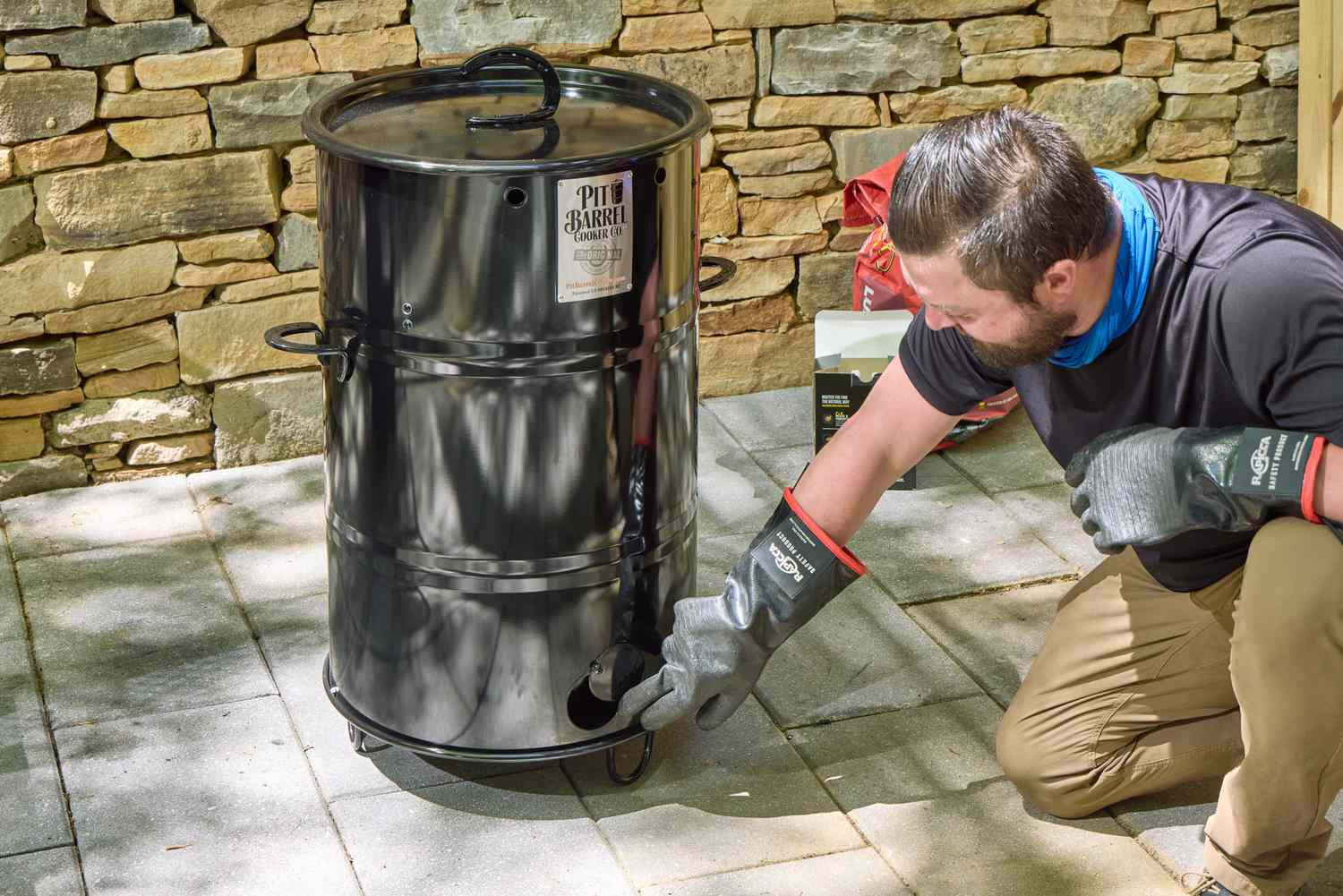 A person opens a vent on the side of the Pit Barrel Cooker Co. Classic Pit Barrel Cooker