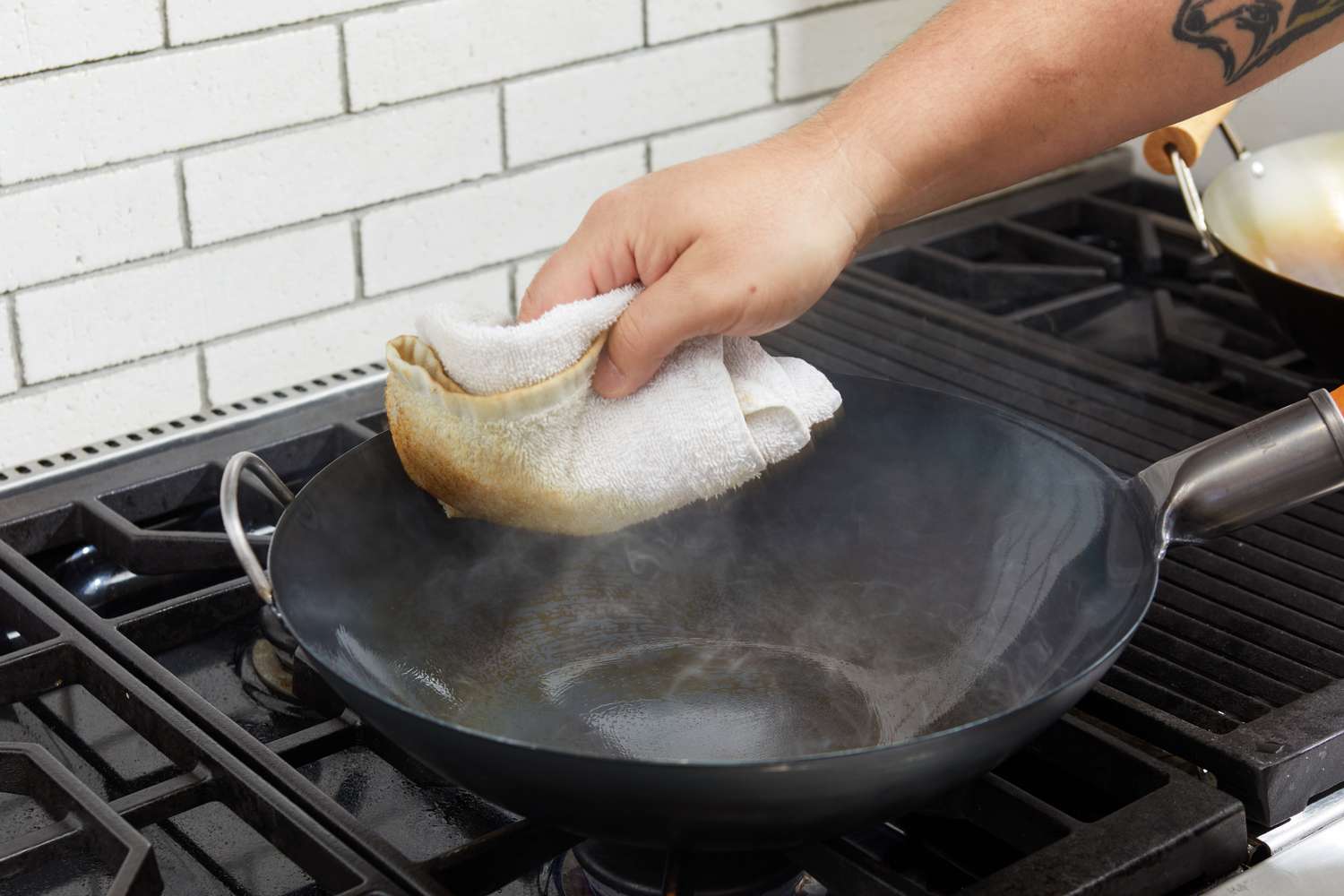 Hand wiping seasoning oil out of a Yosukata Carbon Steel Wok Pan with a white towel 