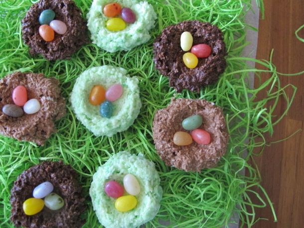 Overhead view of nine chocolate coconut nests with jelly bean eggs. Some nests are dark chocolate, some milk chocolate, as well as green-tinted white chocolate.