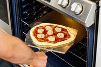 An unbaked pizza on a pizza peel being transferred to a baking steel.