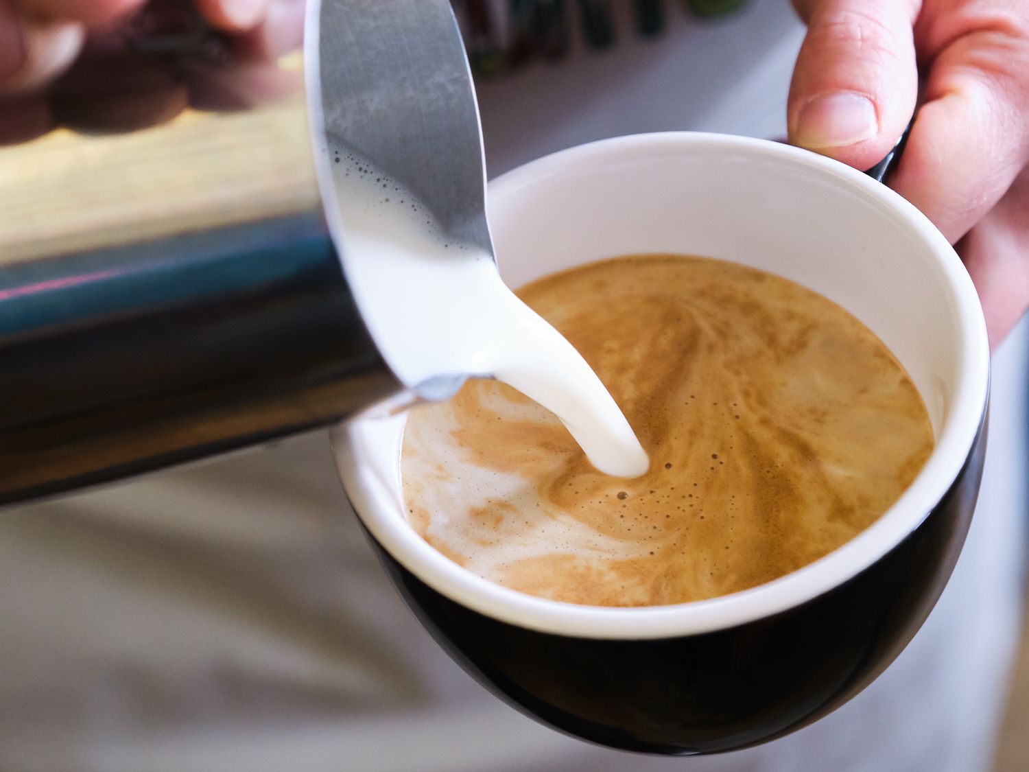 Non-dairy milk being poured into an espresso drink from a pitcher. 