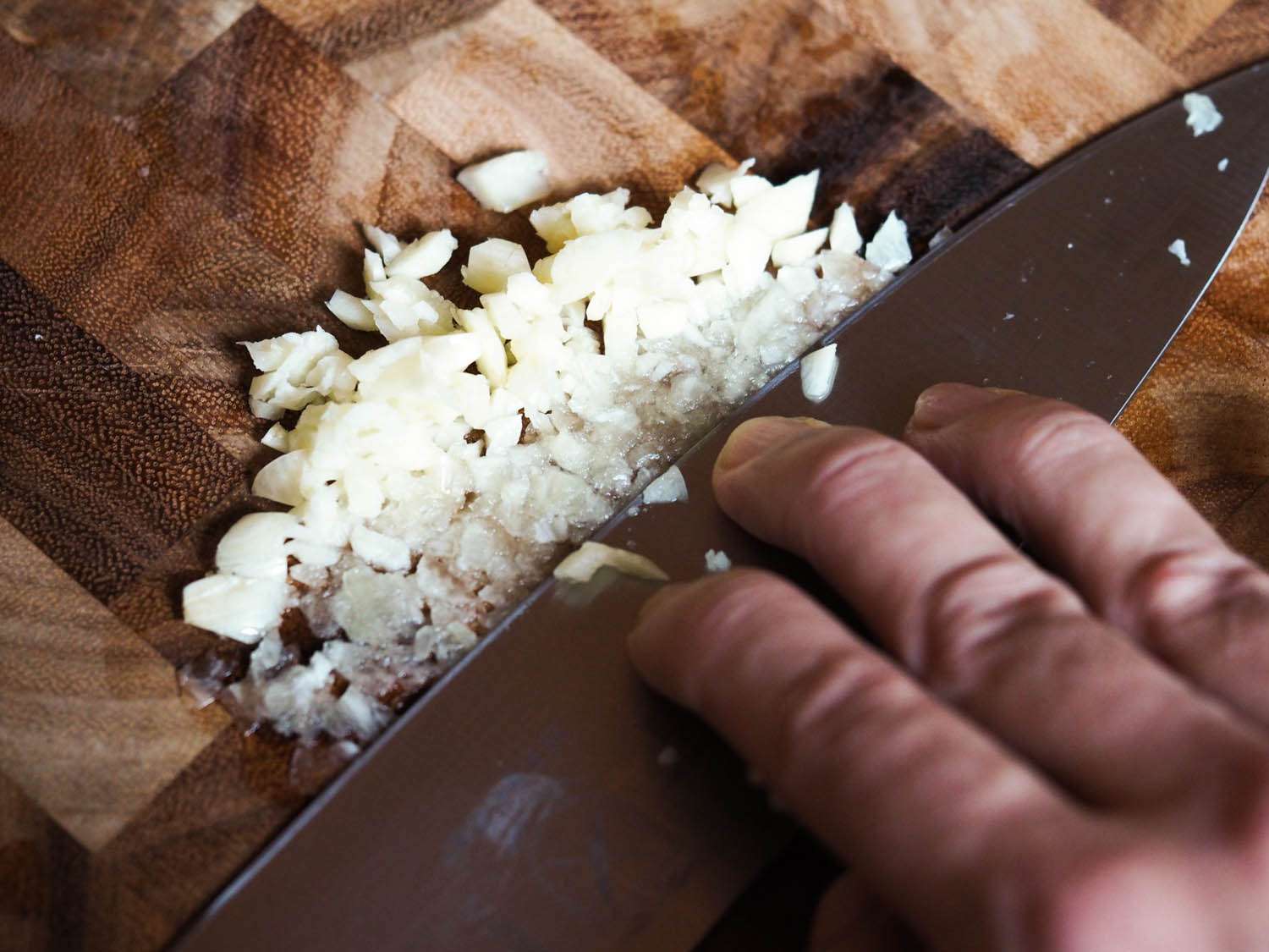 Chopped garlic is mashed with the flat surface of a chef's knife.