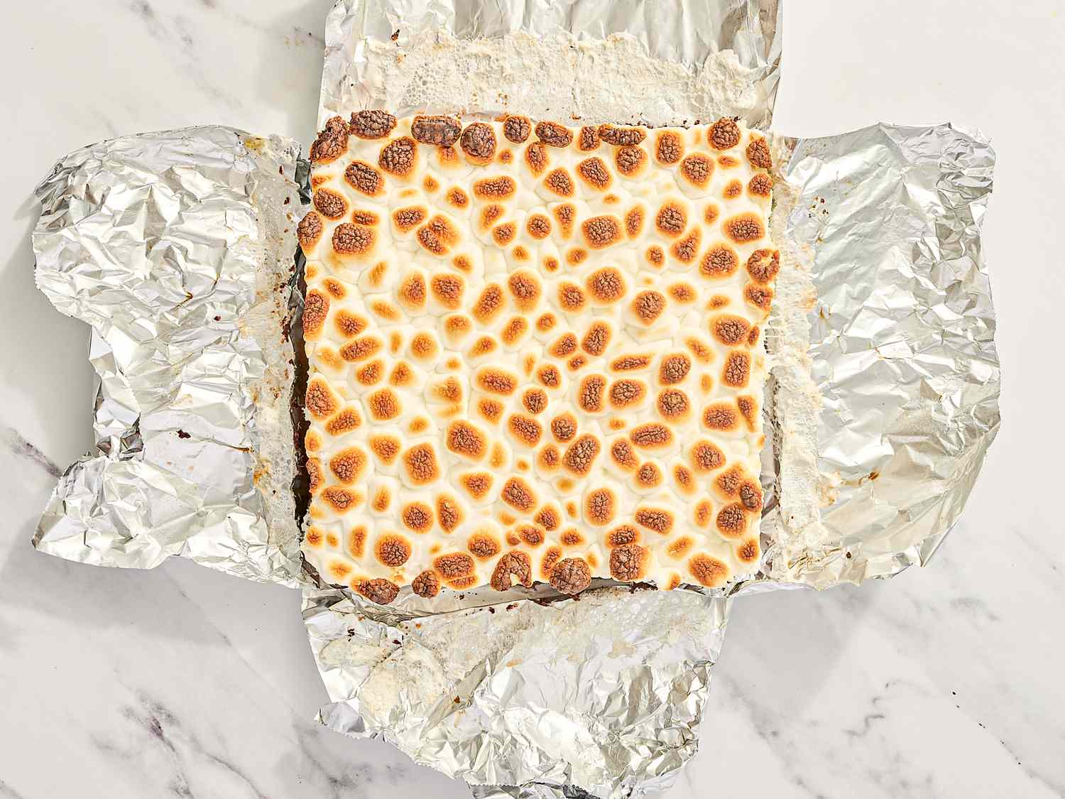 A smores brownie with toasted marshmallows on top resting on aluminum foil