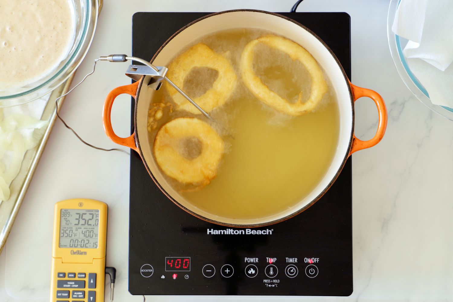 Donuts being fried in oil in a Dutch oven on a portable induction burner.