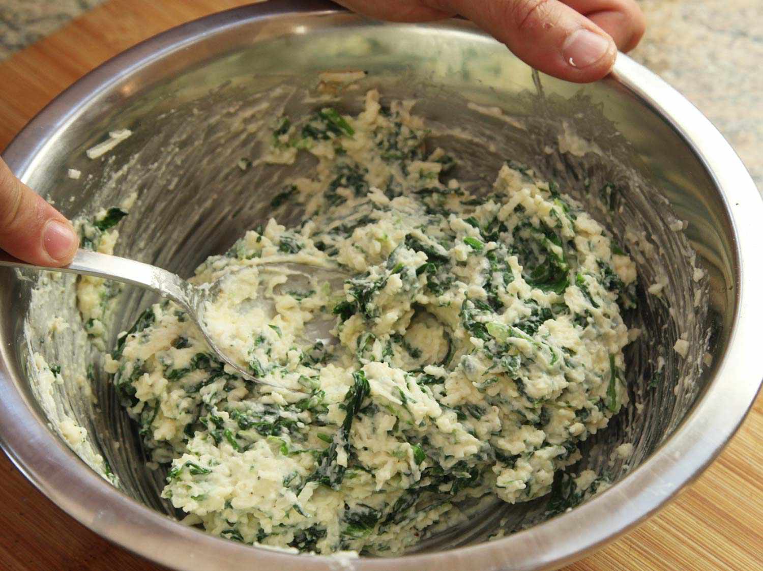 Mixing spinach and arugula with cheese mixture and spices in a mixing bowl. 