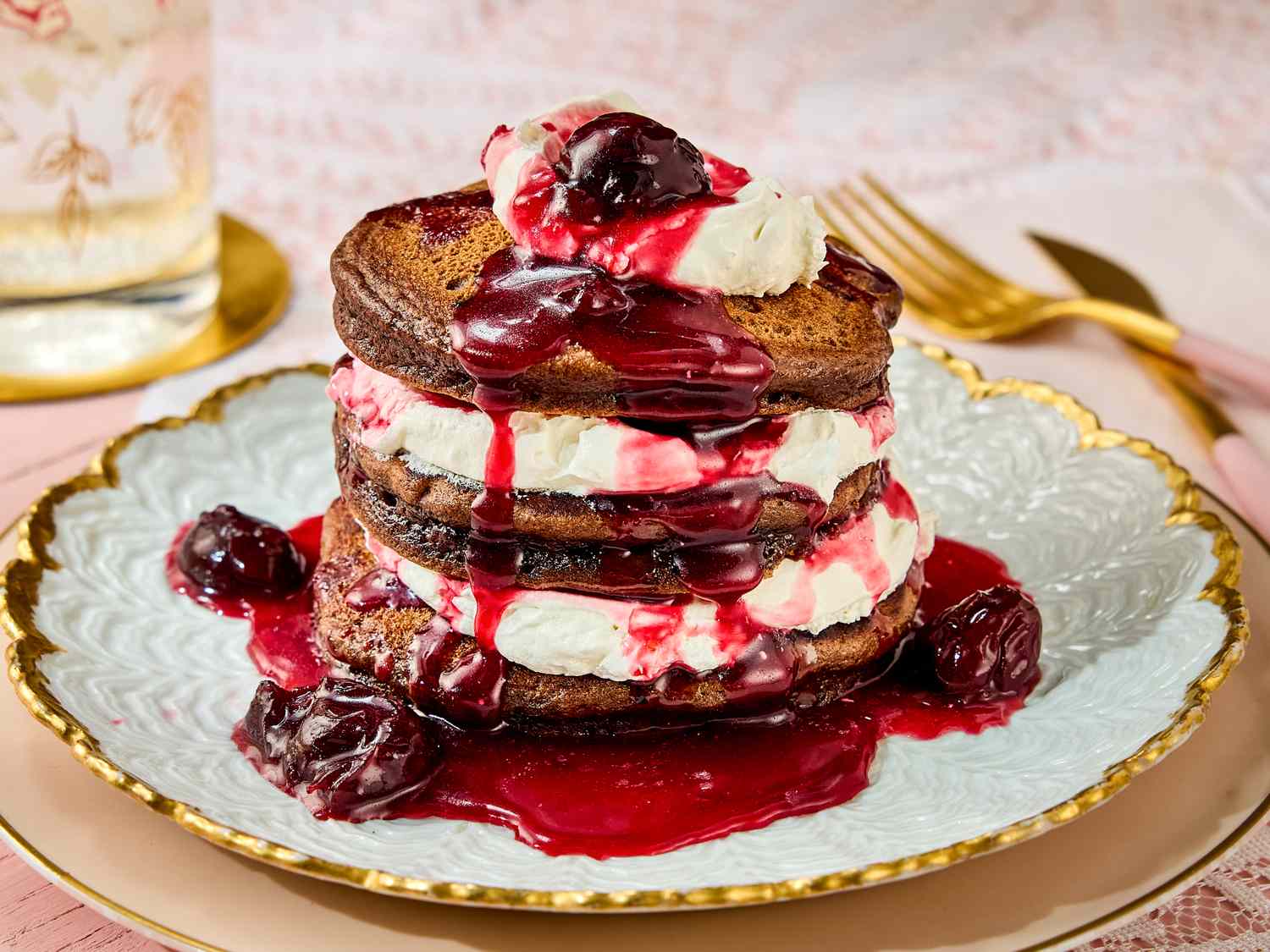 A plate of pancakes layered with whipped cream and topped with cherry sauce and cherries