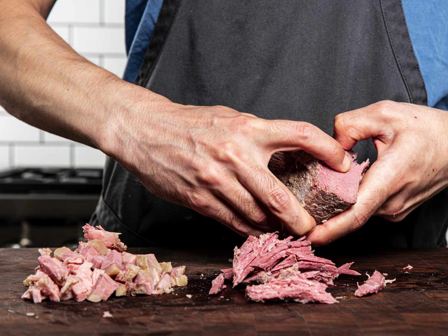 Hands ripping corned beef into piles on a wood surface