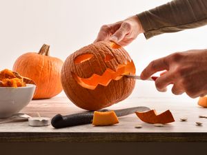 A person carving a jackolantern face on a pumpkin using a knife