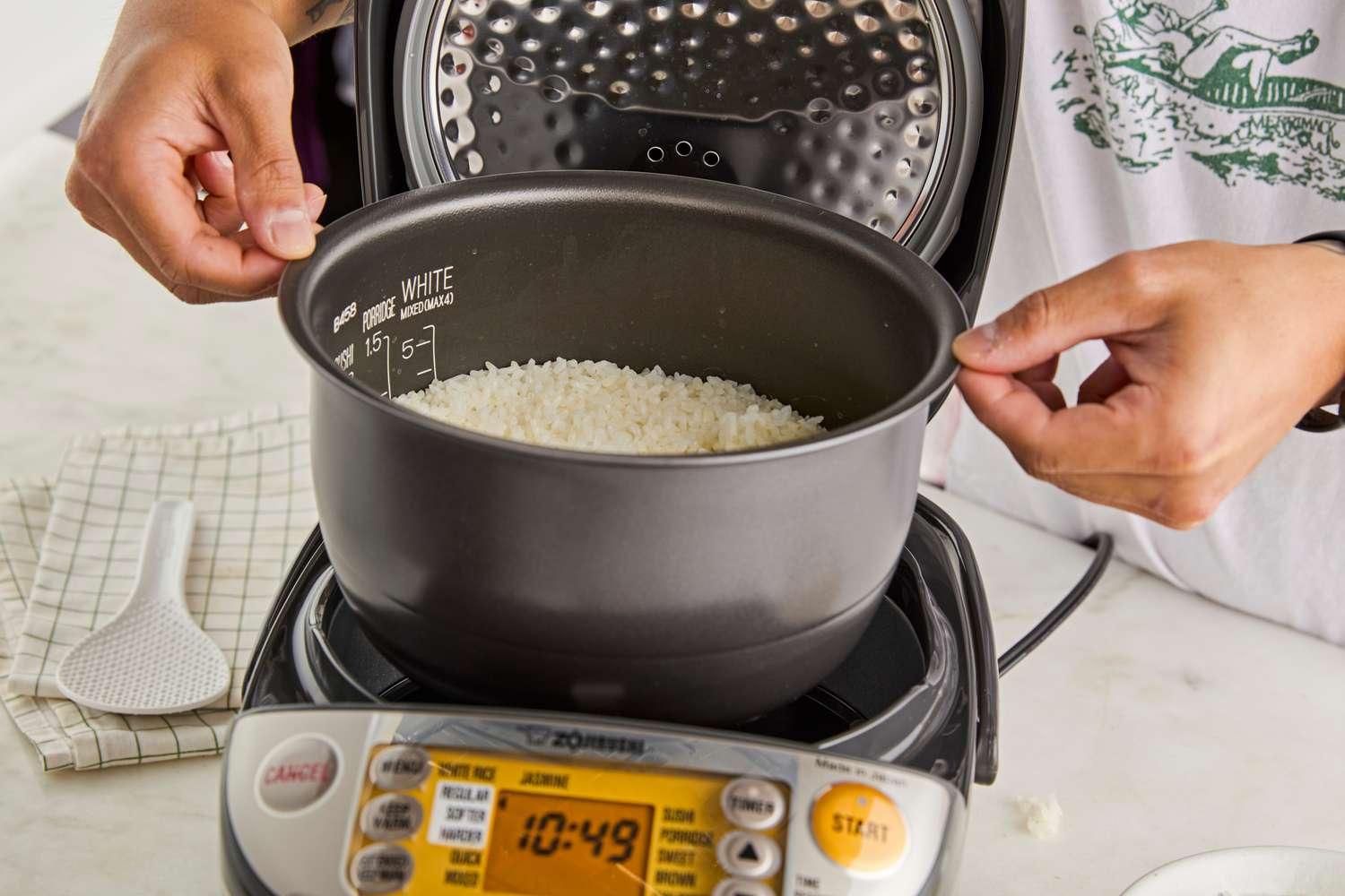 A person lifting the rice cooker pot with cooked rice in it out of the Zojirushi rice cooker.