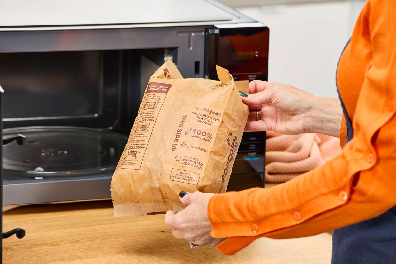 A person holding a bag of popcorn in front of the Magic Chef 1.1 Microwave