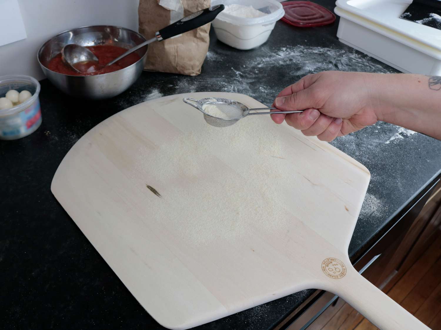 A hand dusting a wooden pizza peel with semolina flour 