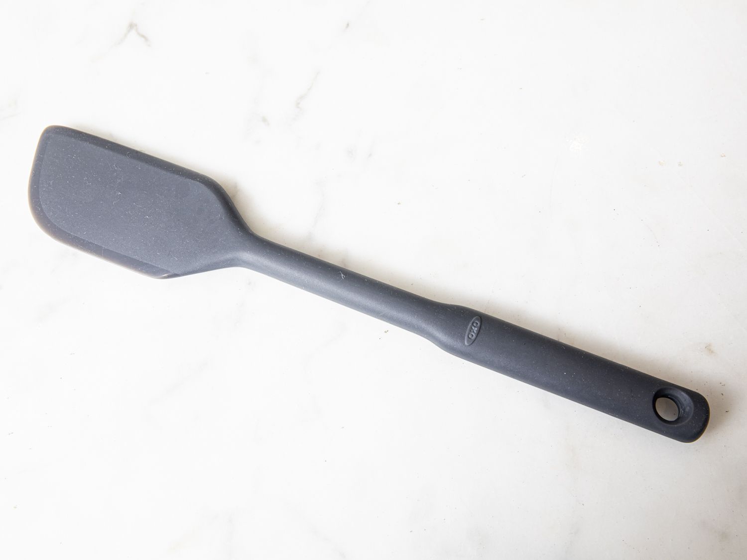 A grey OXO silicone spatula on a marble surface