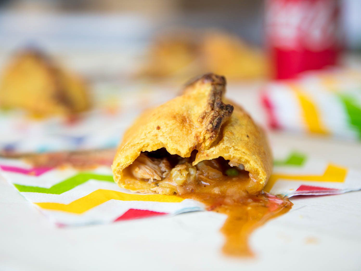 Closeup of a half-devoured salteña, its filling oozing onto a napkin.