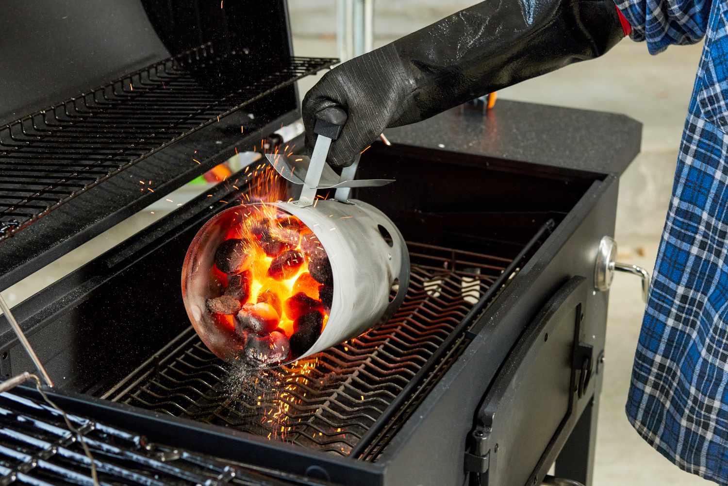 A person adding charcoal to a charcoal grill