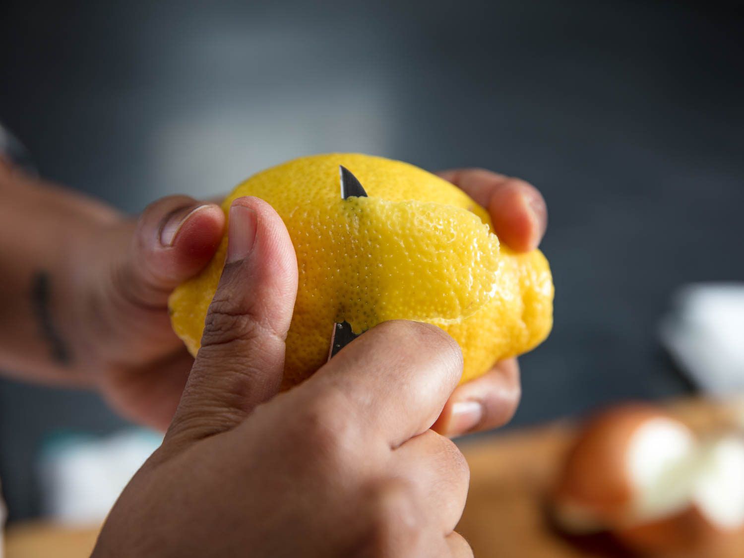 Author uses a tourné knife to slice off a section of lemon zest.