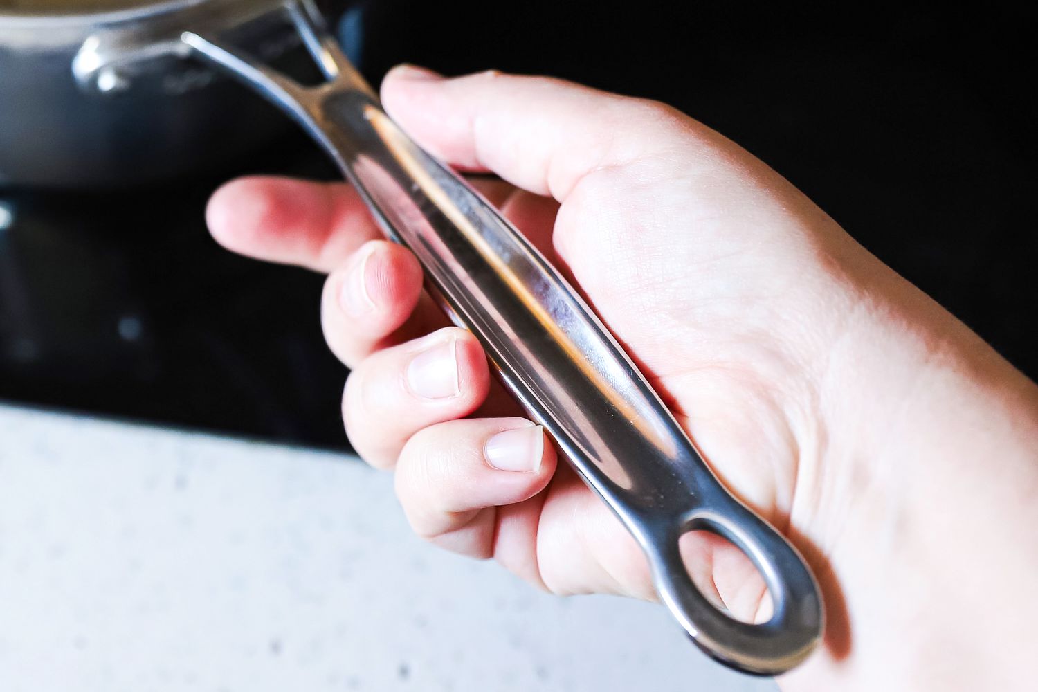 A hand holding the handle of a pot from the Goldilocks 7-piece Cookware Set