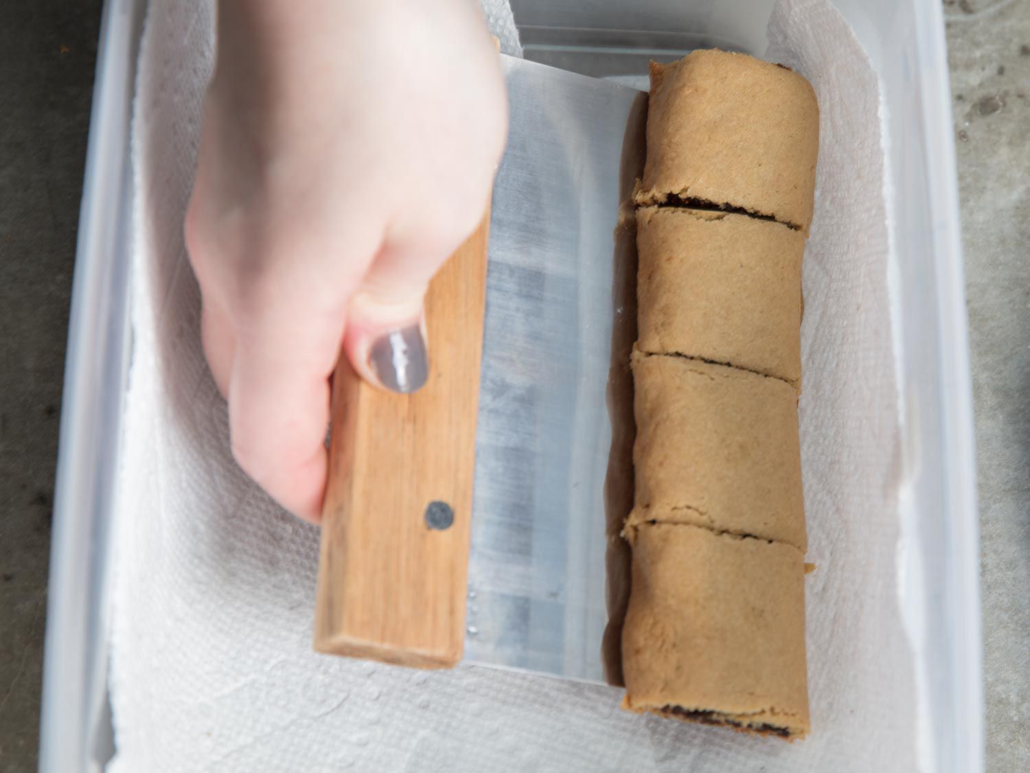 Transferring warm fig newtons with bench scraper into an air-tight container lined with paper towel.