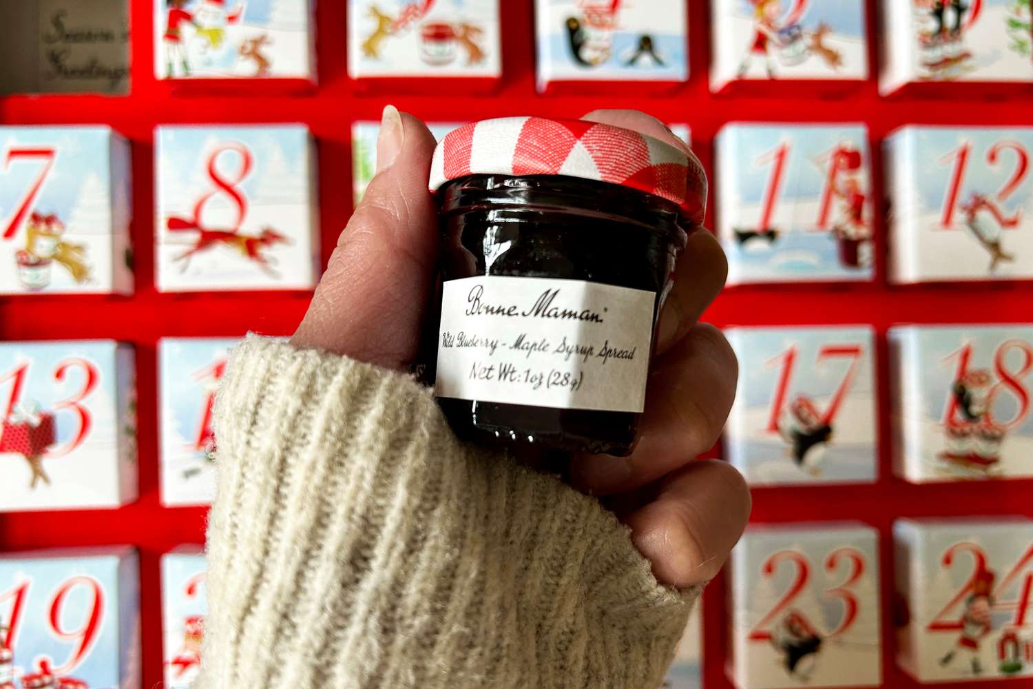 a hand holding a mini jar of Bonne Maman jar in front of the 2025 advent calendar