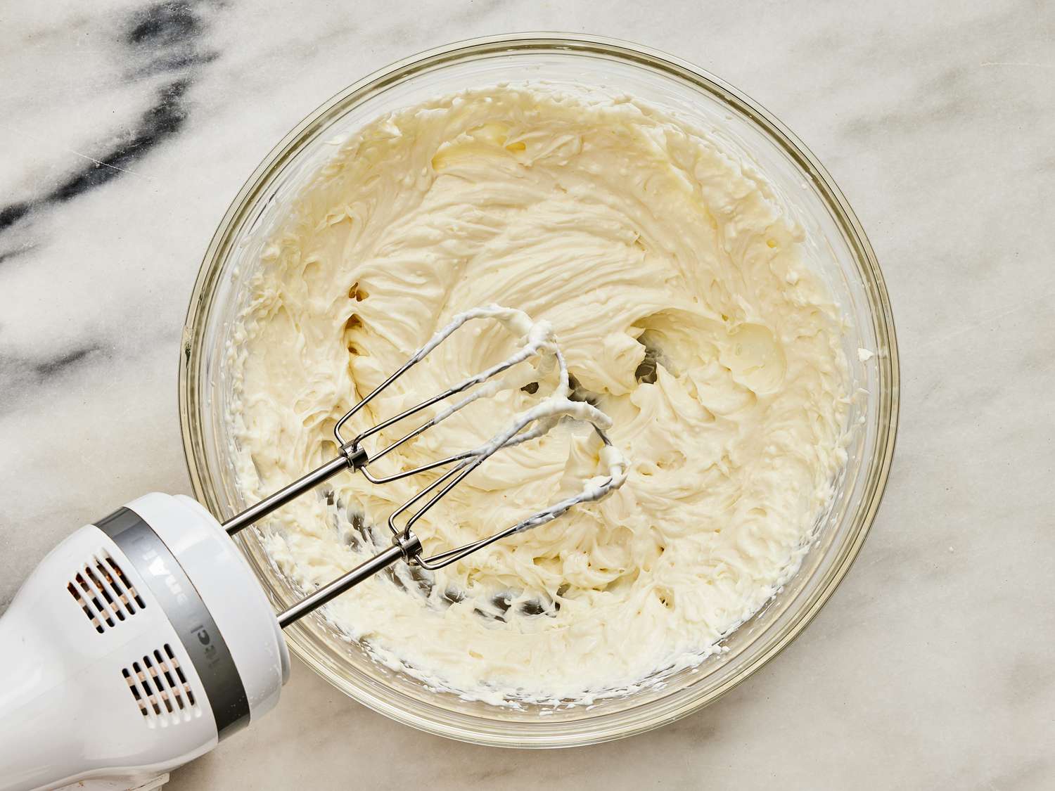 Dressing in a glass bowl being mixed by a hand mixture 