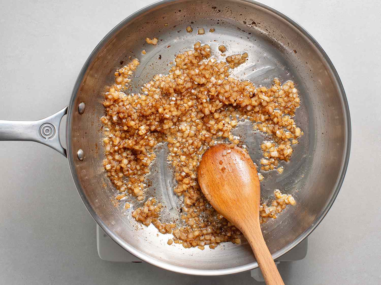 Onions being cooked in bacon fat in a stainless steel skillet.
