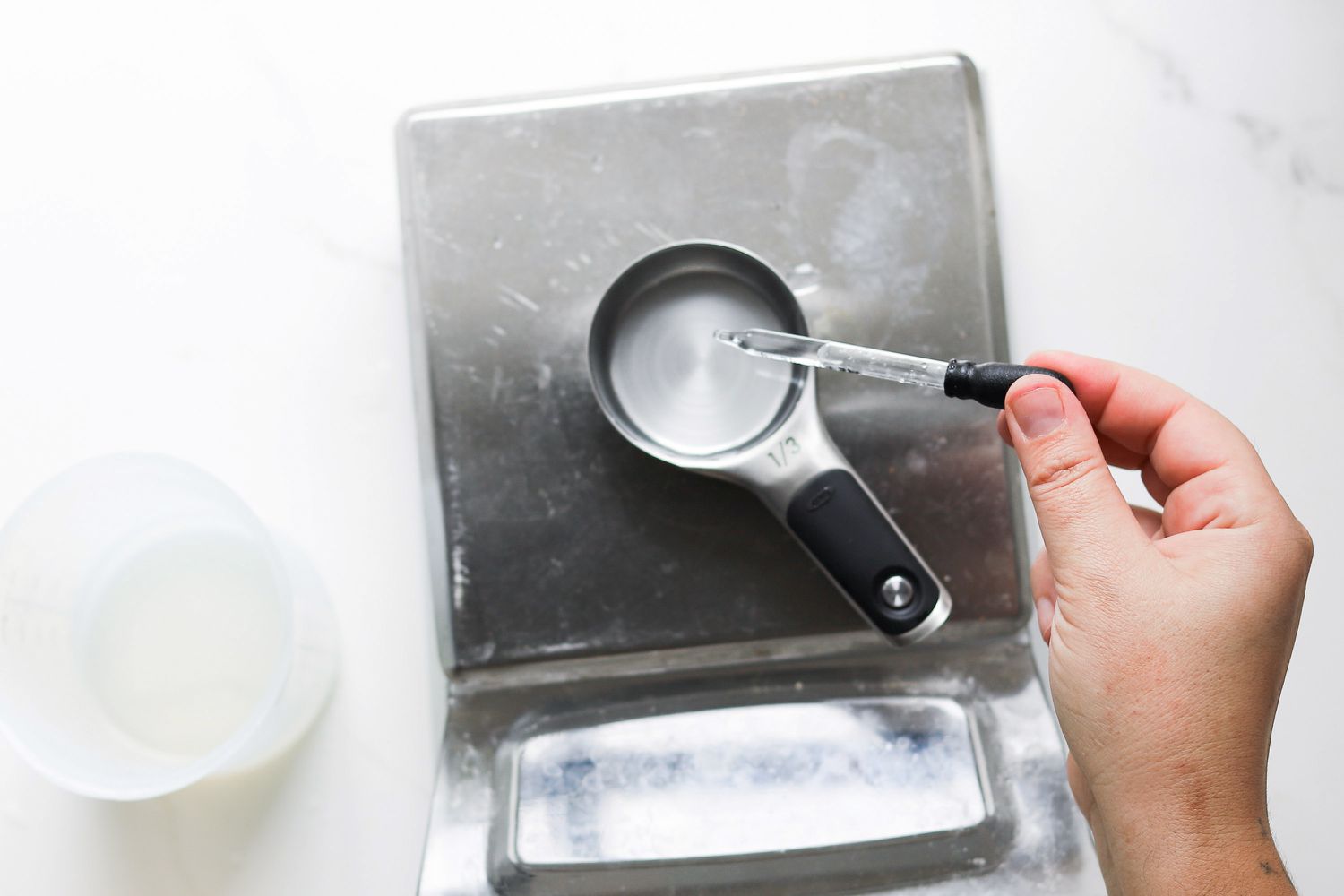 A person using a pipette to add water to a measuring cup set on a scale.