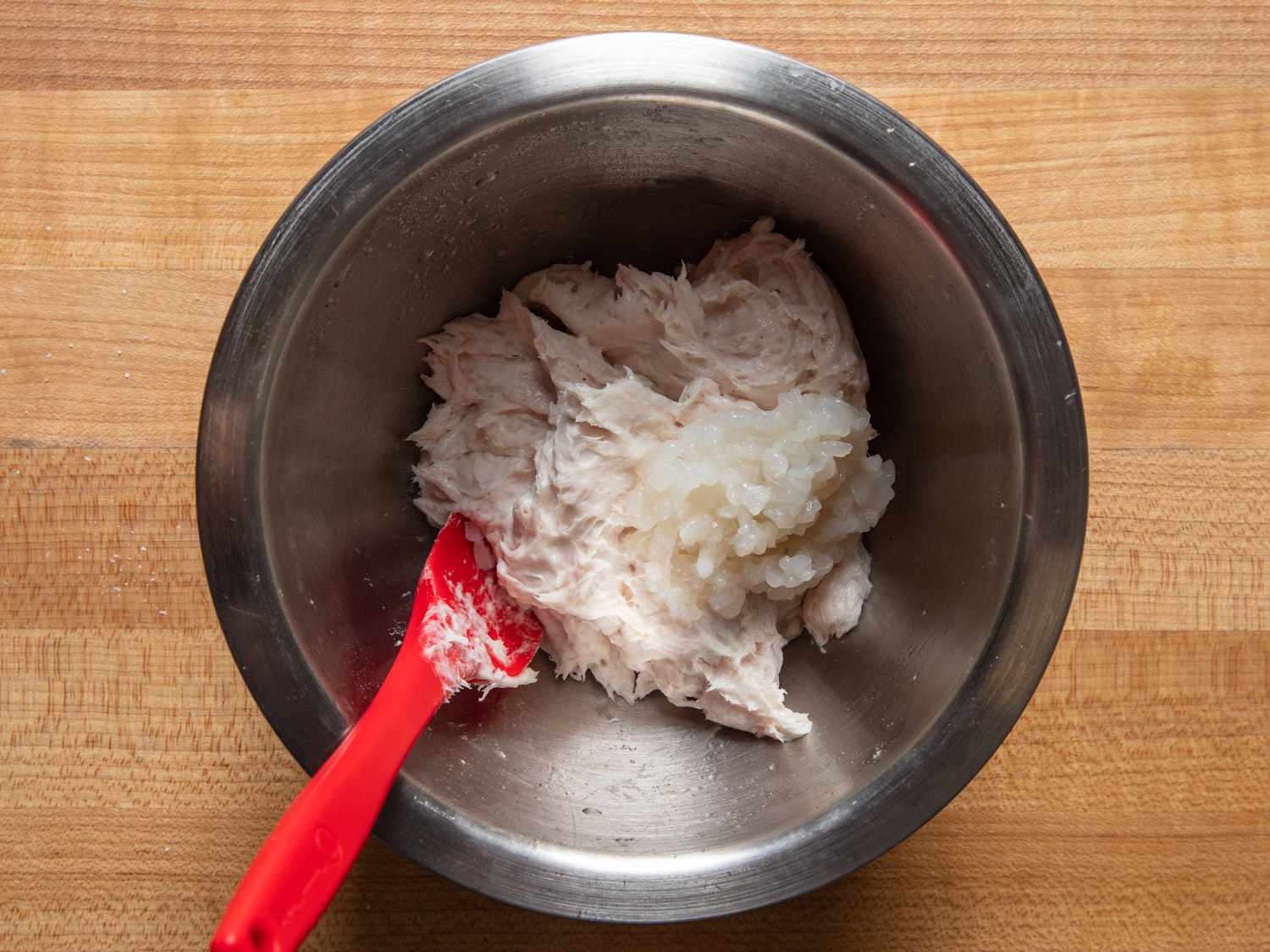 Overhead view of processed squid mixture and minced squid in a bowl with a red spatula