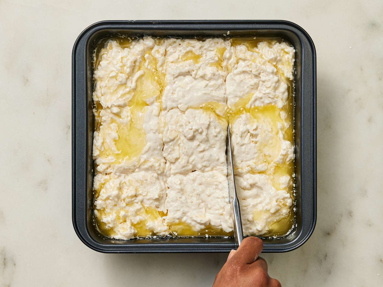 Dough being cut with knife in pan on marble surface 