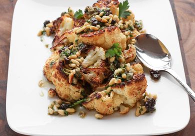 Closeup of Roasted Cauliflower With Pine Nut, Raisin, and Caper Vinaigrette, served on a square white plate.