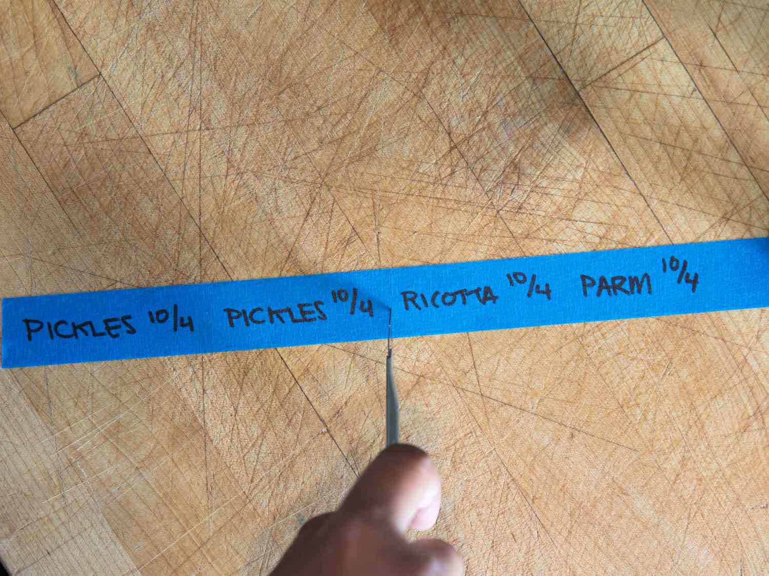 Dividing a strip of blue tape, marked with labels and dates for various foods, using a utility knife