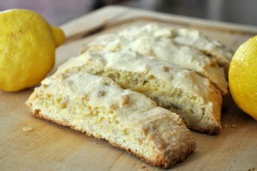 Closeup of lemon pine nut biscotti on a cutting board, flanked by two lemons.