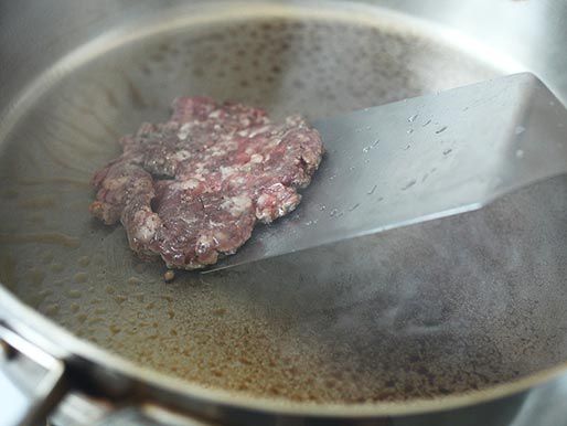 Scraping up a smashed hamburger patty before flipping it on a smoking hot stainless steel skillet.
