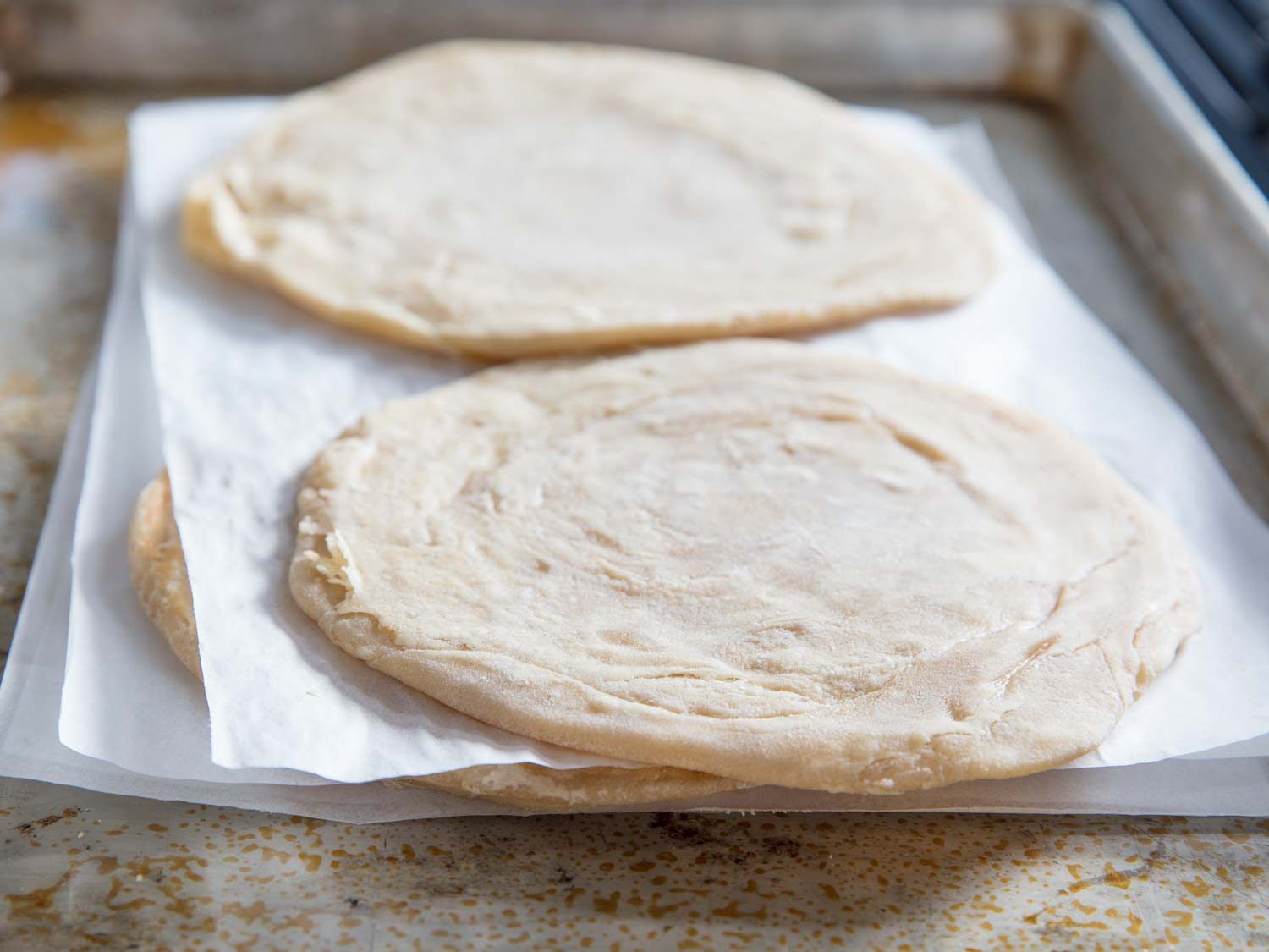 A stack of parcooked parathas, separated with parchment paper.