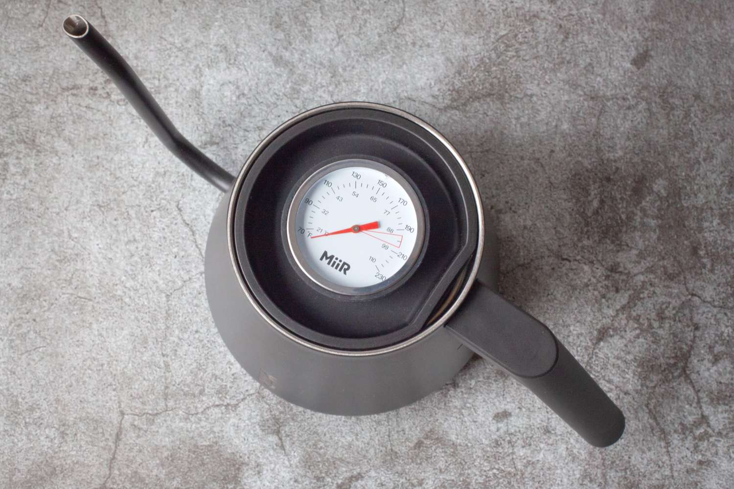 A kettle with an inset thermometer showing temperature viewed from above on a textured surface