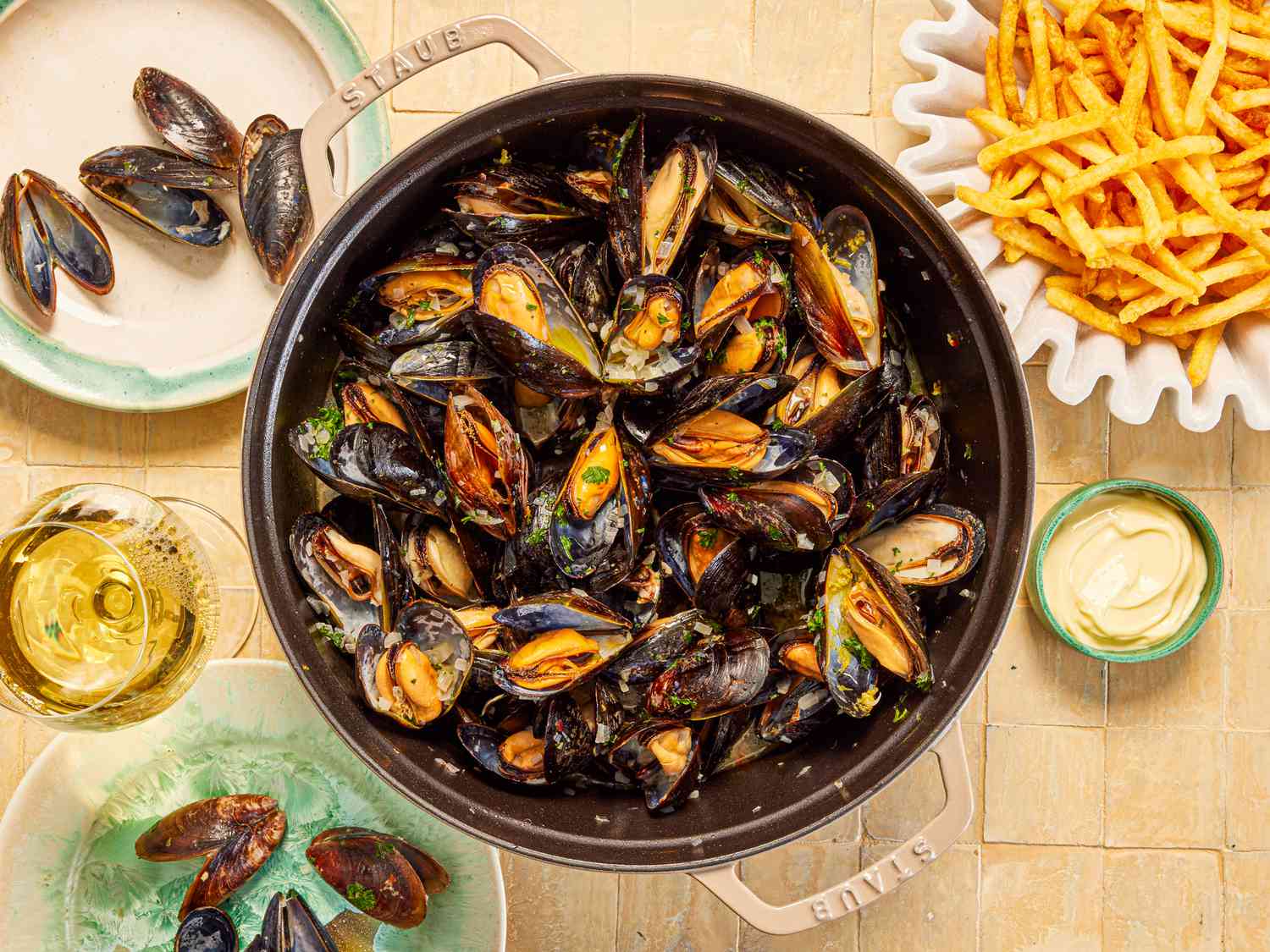 Mussles in a grey Staub Dutch oven and a side of fries.