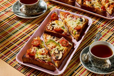 Slices of pizza toast arranged on a tray with cups of tea