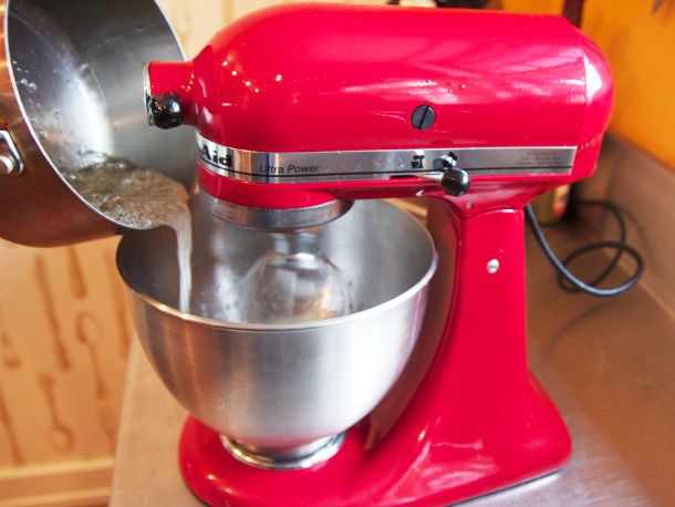 Pouring hot sugar syrup into beaten eggs in a red stand mixer to make Italian meringue