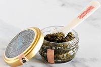 An open jar of Caviar Co osetra caviar with a mother-of-pearl spoon inside