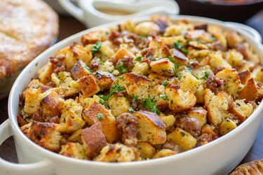A dish of stuffing with herbs and bread cubes on a table with other dishes