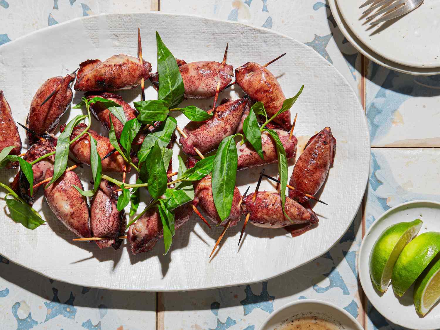 Platter of grilled stuffed squid with garnish displayed on a table with lime wedges and sauce